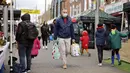 Seorang pria yang mengenakan masker membawa tas belanjaan saat melewati kios-kios di Walthamstow Market, London, Minggu (22/11/2021). Indeks Harga Konsumen Inggris naik ke angka 4,2 persen dalam 12 bulan hingga Oktober 2021, mencapai level tertinggi sejak November 2011. (Tolga Akmen/AFP)