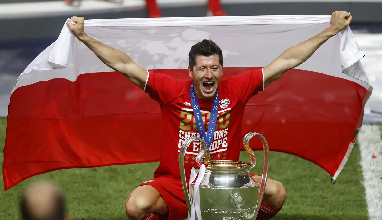 Penyerang Bayern Munchen, Robert Lewandowski berpose dengan bendera Polandia dan trofi Liga Champions setelah mengalahkan PSG pada pertandingan final di stadion Luz di Lisbon (23/8/2020). Munchen menang tipis atas PSG 1-0. (AFP/Pool/Matthew Childs)