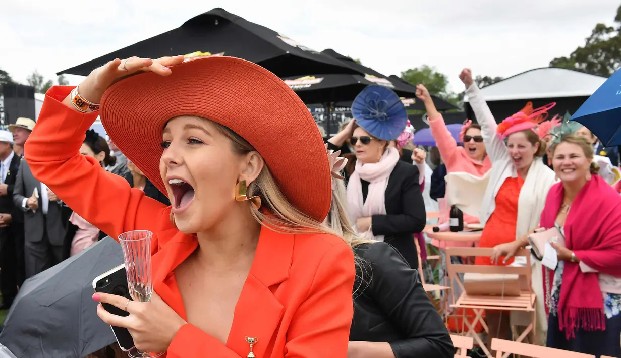 Seorang wanita bersorak saat menyaksikan balap kuda di Race 4 di Melbourne Cup di Flemington Racecourse di Melbourne, Australia, (7/11). Para wanita ini tampil cantik dengan hiasan kepala yang mereka gunakan. (AP Photo / Andy Brownbill)