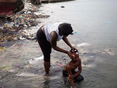 Seorang wanita memandikan putrinya di pantai saat mereka bersiap-siap untuk pergi ke gereja, di Warf of Port Cite Soleil di Port-au-Prince, Haiti (17/3). Cité Soleil merupakan lingkungan yang sangat miskin dan padat penduduk. (AP Photo/Dieu Nalio Chery)