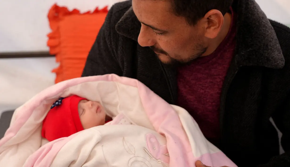 Khalil al-Suwadi menggendong keponakannya Afraa, bayi Suriah yang lahir di bawah reruntuhan setelah gempa bumi 6 Februari yang melanda Turki dan Suriah yang menewaskan orang tua dan saudara kandungnya, di kota Jindayris yang dikuasai pemberontak di Suriah utara, Selasa (21/2/2023). Kini, bayi yang diberi nama Afraa al-Suwadi tersebut diasuh oleh pamannya. (Rami al SAYED / AFP)