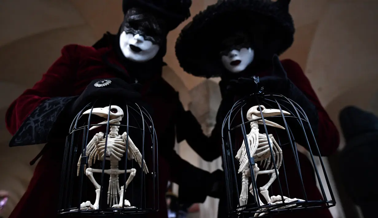 Peserta mengenakan kostum dan topeng membawa aksesoris replika kerangka burung saat mengikuti karnaval tradisional Venesia di Italia (27/1). (AFP Photo/Filippo Monteforte)