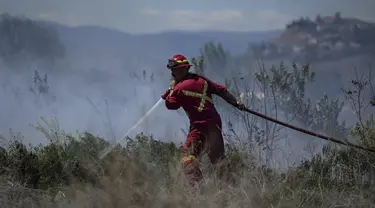 Seorang petugas pemadam kebakaran mengarahkan air ke api rumput di areal di belakang properti perumahan di Kamloops, British Columbia, Senin, 5 Juni 2023. Tidak ada bangunan yang rusak tetapi petugas pemadam kebakaran harus menghadapi kondisi angin yang sangat kencang saat memadamkan api. (Darryl Dyck/The Canadian Press via AP)