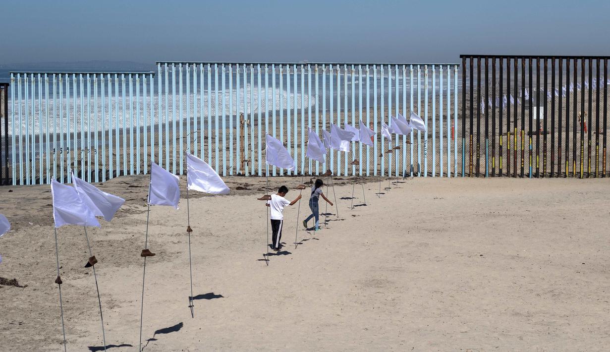 Dua orang anak bermain di seni instalasi kontemporer "Tu huella es el camino, tu bandera es de paz" di Playas de Tijuana, Meksiko (7/10). Karya ini bentuk penghormatan untuk para migran yang melintasi perbatasan Meksiko-AS. (AFP Photo/Guillermo Arias)