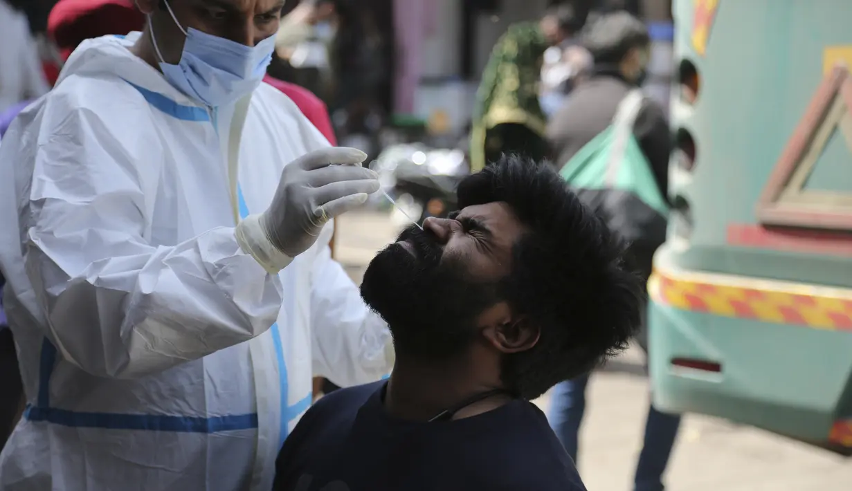 Seorang petugas kesehatan mengumpulkan sampel swab penumpang untuk diuji COVID-19 di sebuah terminal bus di Jammu, India (26/3/2021).  Negara bagian telah memberlakukan lockdown di beberapa distrik hingga akhir bula. (AP Photo/Channi Anand)
