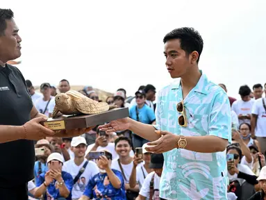 Calon Wakil Presiden nomor urut 2 Gibran Rakabuming Raka (kanan) menerima ukiran penyu saat rapat umum kampanyenya di pantai Sanur, Bali pada 27 Januari 2024. (SONNY TUMBELAKA/AFP)