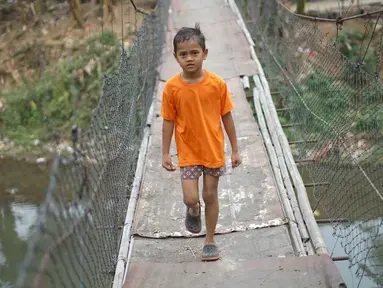 melintasi jembatan gantung semi permanen di kawasan Srengseng Sawah, Jakarta Selatan, Sabtu (24/8/2019). Jauhnya akses penyeberangan lain menyebabkan warga terpaksa memanfaatkan jembatan tersebut untuk menyeberangi Sungai Ciliwung. (Liputan6.com/Immanuel Antonius)