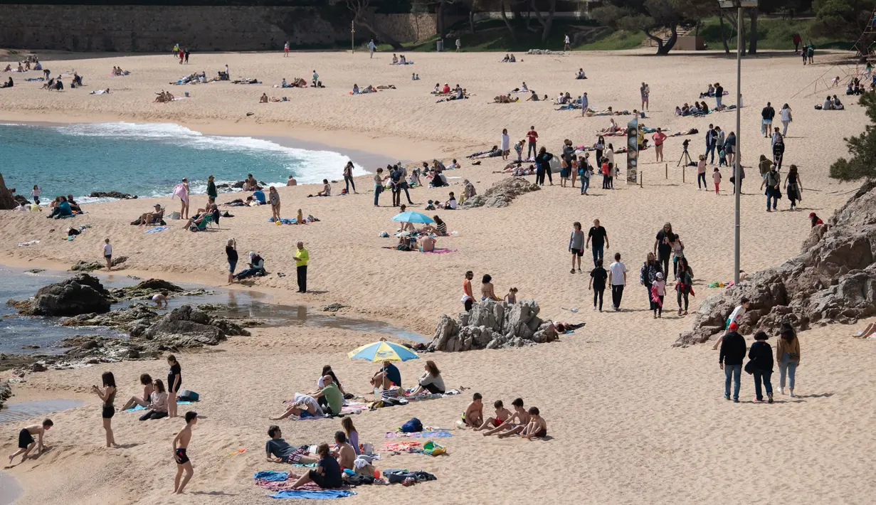 Orang-orang menikmati hari yang cerah di pantai Sa Conca di Castell-Platja D'Aro dekat Girona, Spanyol pada Rabu (31/3/2021). Masker telah wajib digunakan di Spanyol sejak Mei 2020 namun hanya di tempat yang tidak memungkinkan menjaga jarak minimal 2 meter. (Josep LAGO / AFP)