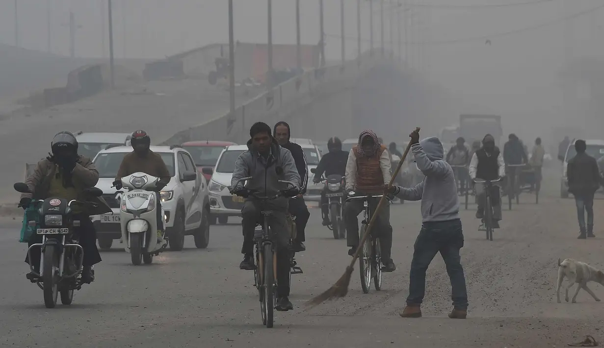 Seorang pekerja India dengan Delhi Municipal Corporation menyapu jalan saat kendaraan melewati pagi yang berkabut dingin di New Delhi, India (2/1). (AFP Photo/Prakash Singh)