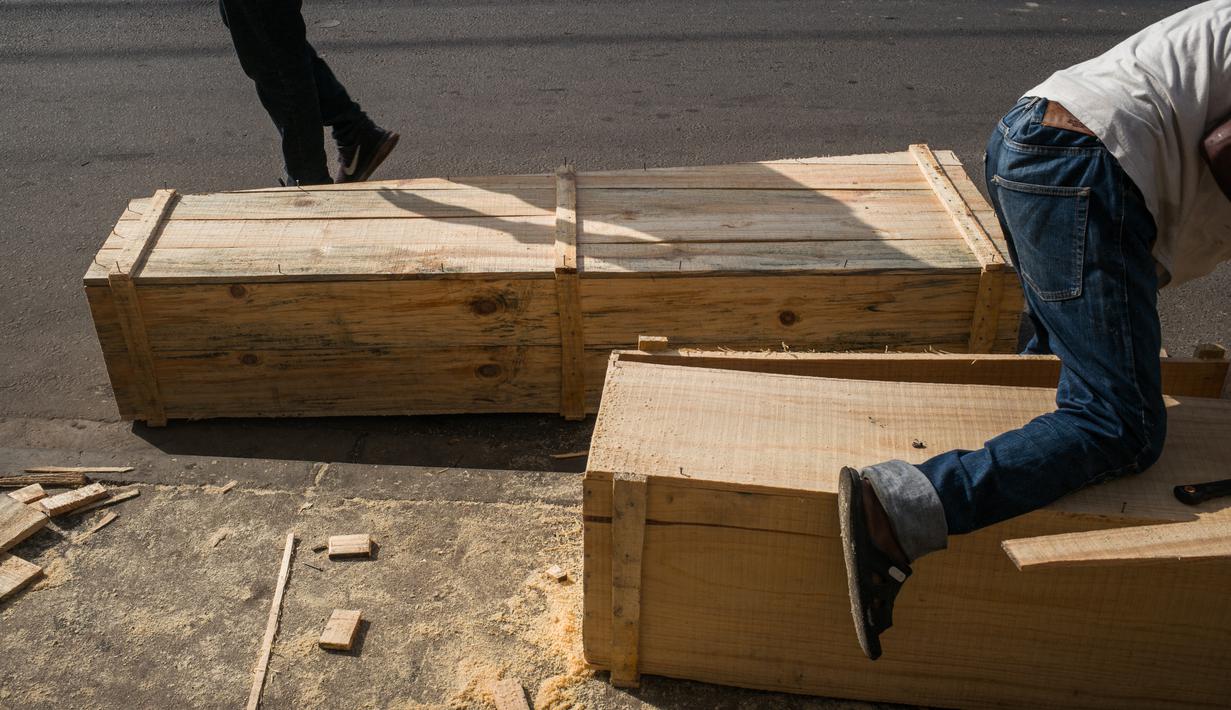 Mr. Jean dan timnya membuat peti mati murah di jalan, padahal kegiatan ini dilarang di jalan raya umum, di Antananarivo, Rabu (14/4/2021). Sejak gelombang kedua Covid-19 di Madagaskar, yang menyebabkan jumlah kematian meningkat di ibu kota, permintaan peti mati juga meningkat pesat. (RIJASOLO/AFP)