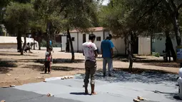 Seorang anak mengamati imigran yang sedang melaksanakan salat pada hari pertama Ramadan, di kamp pengungsian milik pemerintah Yunani di Schisto, Athena, Senin (6/6). Imigran membuat masjid darurat di sebuah halaman terbuka. (REUTERS/Alkis Konstantinidis)