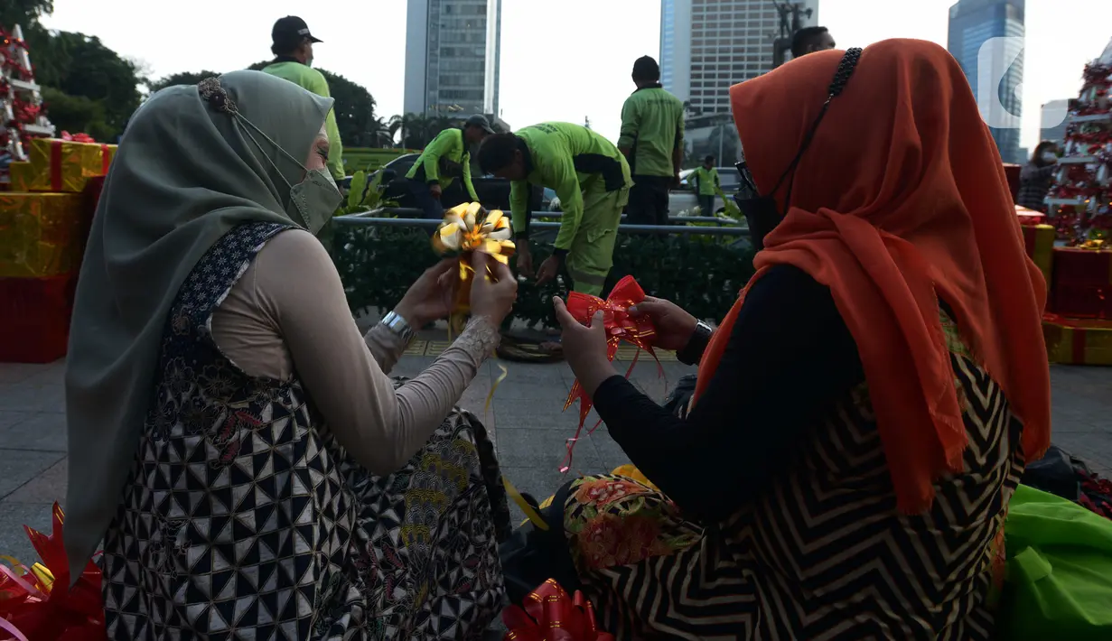 Dua wanita menghias dekorasi Natal di Bundaran HI, Jakarta, Kamis (23/12/2021). Christmas Carol dilakukan di tujuh titik yang pada hari ini memasang pohon Natal di beberapa titik tersebut. (merdeka.com/Imam Buhori)