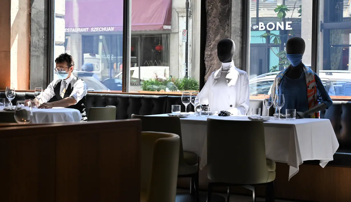 Pramusaji menata meja di dekat maneken yang diletakkan untuk menjaga jarak di sebuah restoran di Old Montreal, Kanada pada 10 Juli 2020. Restoran ini menempatkan maneken untuk menjaga jarak konsumen dan didandani dengan baju-baju keluaran terkini yang dapat dibeli pengunjung. (Eric THOMAS/AFP)