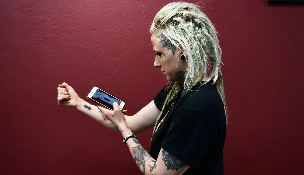 Hanna Washlake mendengarkan tato gelombang suara yang mengeluarkan pesan dari ibunya di Black Raven Tattoo California, 12 April 2018. Soundwave Tattoo menghasilkan suara berdurasi satu menit yang berasal dari pola gelombang audio. (AFP/FREDERIC J. BROWN)