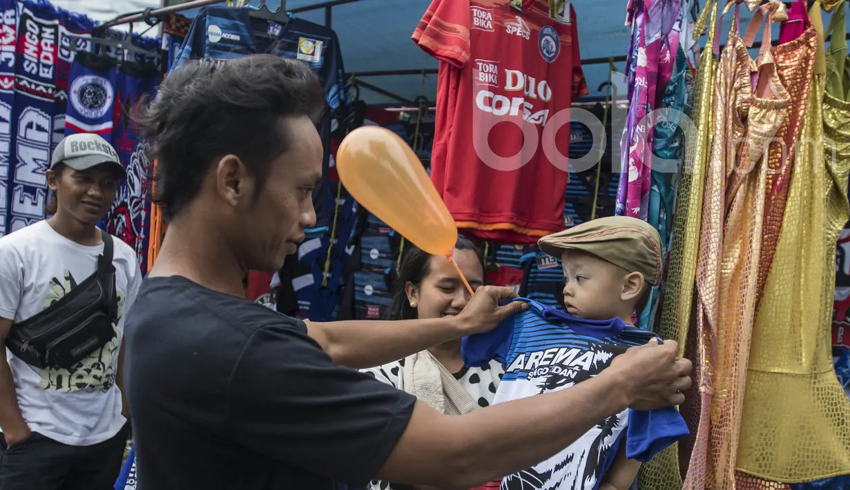 Seorang bapak mencobakan anaknya baju yang dijual oleh pedagang kaki lima jelang laga semifinal Piala Presiden 2017 antara Arema FC melawan Semen Padang di sekitar Stadion Kanjuruhan, Malang, Jawa Timur, Minggu (5/3/2017). (Bola.com/Vitalis Yogi Trisna)