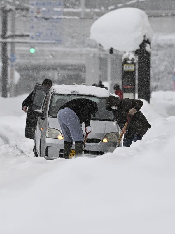 Orang-orang menyekop salju di sekitar mobil yang terjebak di salju di Toyama, di pesisir Laut Jepang, Senin (11/1/2021). Sekitar 1000 kendaraan terjebak di jalan raya bersalju di kota Sakai pada pagi hari, sementara 200 mobil lainnya terdampar di jalan raya di tengah salju tebal di kota Nanto. (Kyod
