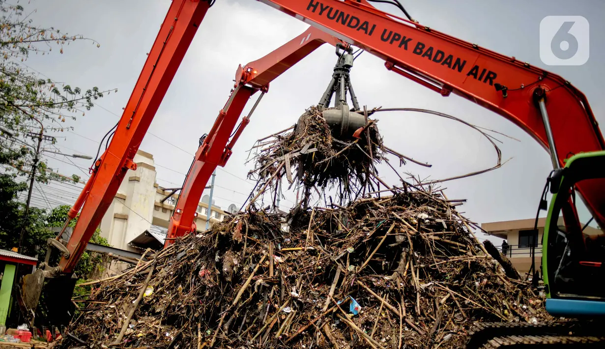 Petugas dibantu alat berat membersihkan sampah kayu dan bambu yang tersangkut di Pintu Air Manggarai, Jakarta, Rabu (9/10/2019). Sampah tersebut merupakan kiriman dari Bogor usai diguyur hujan deras tadi malam. (Liputan6.com/Faizal Fanani)