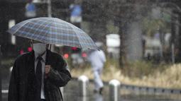Seorang pria yang mengenakan masker berjalan di tengah hujan bersalju di Tokyo, Selasa (22/3/2022). Pemerintah Jepang memperingatkan potensi pemadaman karena kekurangan pasokan listrik akibat tutupnya beberapa pembangkit setelah gempa bumi besar pekan lalu. (AP Photo/Eugene Hoshiko)