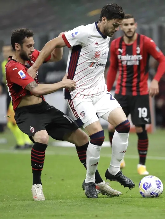 Gelandang AC Milan, Hakan Calhanoglu berebut bola dengan bek Cagliari, Luca Ceppitelli pada pekan ke-37 Serie A di San Siro, Senin (17/5/2021) dini hari WIB.  AC Milan gagal menjauh di klasemen Liga Italia usai imbang 0-0 lawan Cagliari. (AP Photo/Luca Bruno)