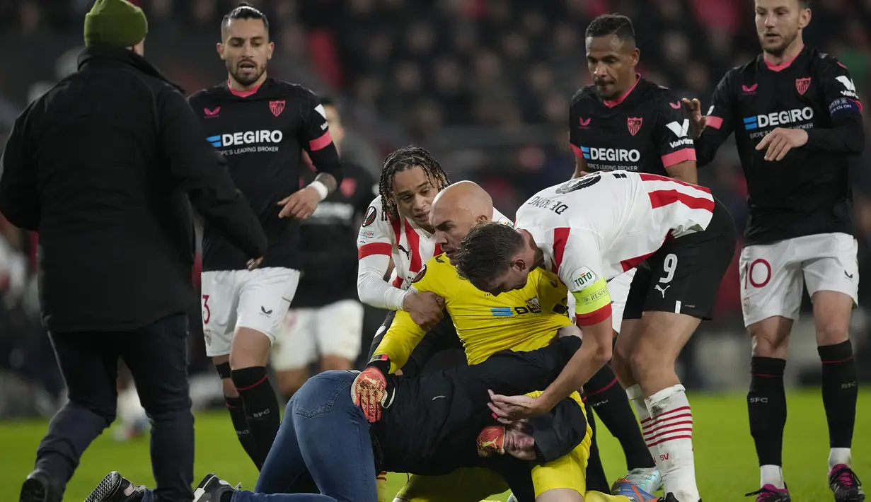 <p>Kiper Sevilla, Marko Dmitrovic berhasil melumpuhkan seorang suporter fanatik PSV yang menyerangnya dalam laga leg kedua babak playoff fase gugur Liga Europa 2022/2023 di Philips Stadium, Eindhoven, Jumat (24/2/2023). (AP Photo/Peter Dejong)</p>