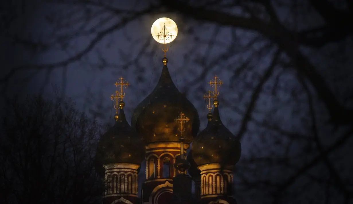 Supermoon terlihat di belakang salib dari gereja Ortodoks Kristen di Moskow, Rusia, Selasa (7/4/2020). Fenomena dimana bulan berada pada titik terdekat dengan bumi ini merupakan penampakan supermoon terbesar di tahun 2020. (AP Photo/Alexander Zemlianichenko)
