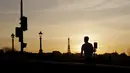 Seorang pria mengendarai skuter listrik dengan Menara Eiffel di latar belakang, saat matahari terbenam, di Paris (29/3/2021). (AP Photo/Thibault Camus)
