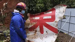 Seorang anggota tim penyelamat membawa potongan puing di lokasi kecelakaan penerbangan China Eastern di Kabupaten Tengxian di Daerah Otonomi Guangxi Zhuang, China selatan (24/3/2022). (Lu Boan/Xinhua via AP)