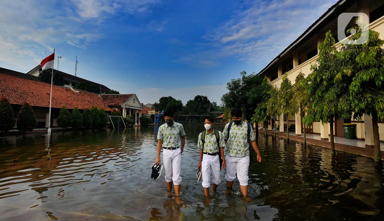 Siswa berjalan melewati banjir yang menggenangi halaman  sekolah di SMAN 4 Tangsel, Pondok Ranji, Tangerang Selatan, Banten, Selasa (14/6/2022). Tiga  pekan lebih banjir merendam lapangan sekolah itu dikarenakan tertutupnya saluran air oleh sampah yang berasal dari tempat pembuangan sampah (TPS) ilegal. (merdeka.com/Arie Basuki)