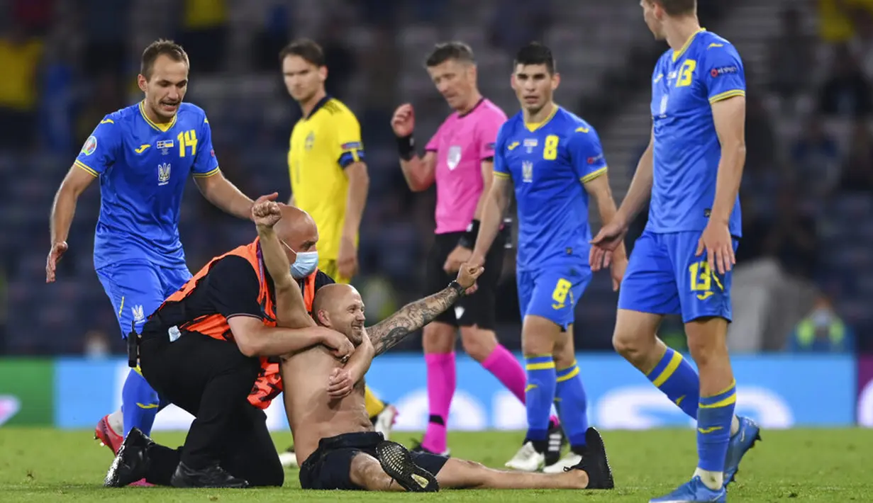 Petugas keamanan menghentikan penyusup yang masuk ke lapangan saat pertandingan babak 16 besar Euro 2020 antara Swedia dan Ukraina di Stadion Hampden Park, Glasgow, Selasa (29/6/2021). Ukraina menang 2-1. (Stu Forster/Pool via AP)