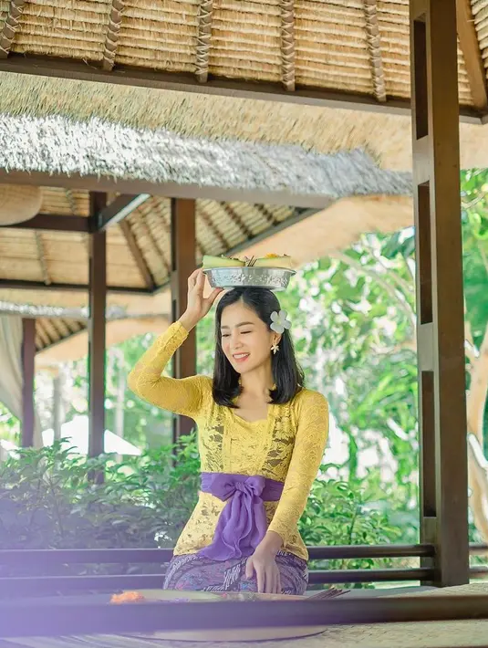 Bunga Zainal tampil cantik menawan dalam balutan kebaya Bali warna kuning dan ungu. Bunga kamboja yang diselipkan pada telinganya membuatnya terlihat lebih anggun. (Instagram/bungazainal05).