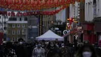 Wanita berjalan melalui Chinatown di Soho di London, Selasa (28/12/2021). Padahal banyak negara Eropa telah memulai pembatasan lebih lanjut pada populasi mereka karena jumlah kasus COVID-19 terkait Omicron meningkat, dan mereka bertujuan untuk menahan penyebaran virus. (AP Photo/Alastair Grant)