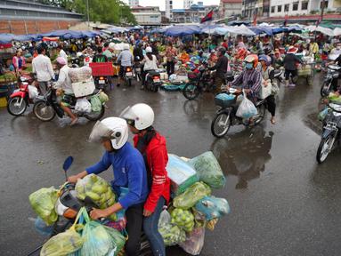 Orang-orang mengendarai sepeda motor melewati pasar di Phnom Penh (24/7/2020). Pasar membentuk bagian integral dalam kehidupan orang Kamboja, dengan kunjungan harian yang dilakukan untuk persediaan makanan untuk hari itu serta barang-barang lainnya. (AFP/Tang Chhin Sothy)