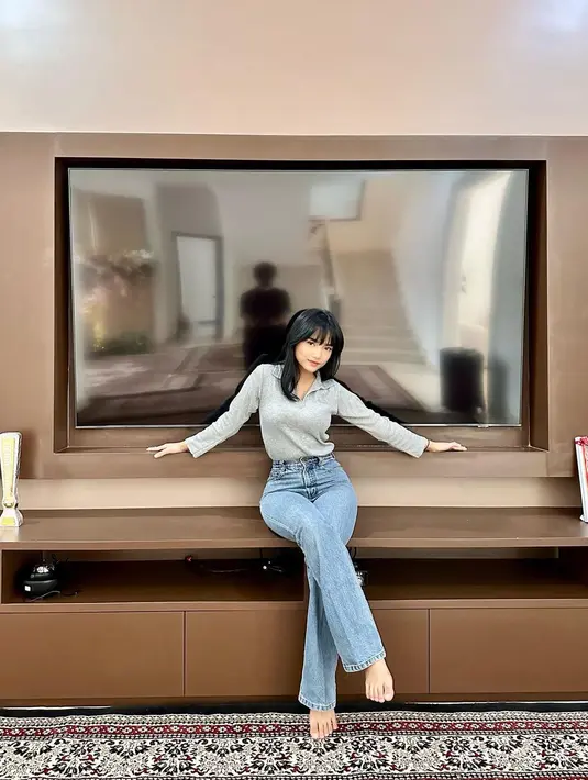 Berpose di depan smart TV super besar, Fuji kembali tampak mengenakan celana jeans. Padu padan atasan abu-abu berkerah lengan panjang dengan celana jeans panjang membuat tubuhnya terlihat ramping dan kaki lebih jenjang. Foto: Instagram.