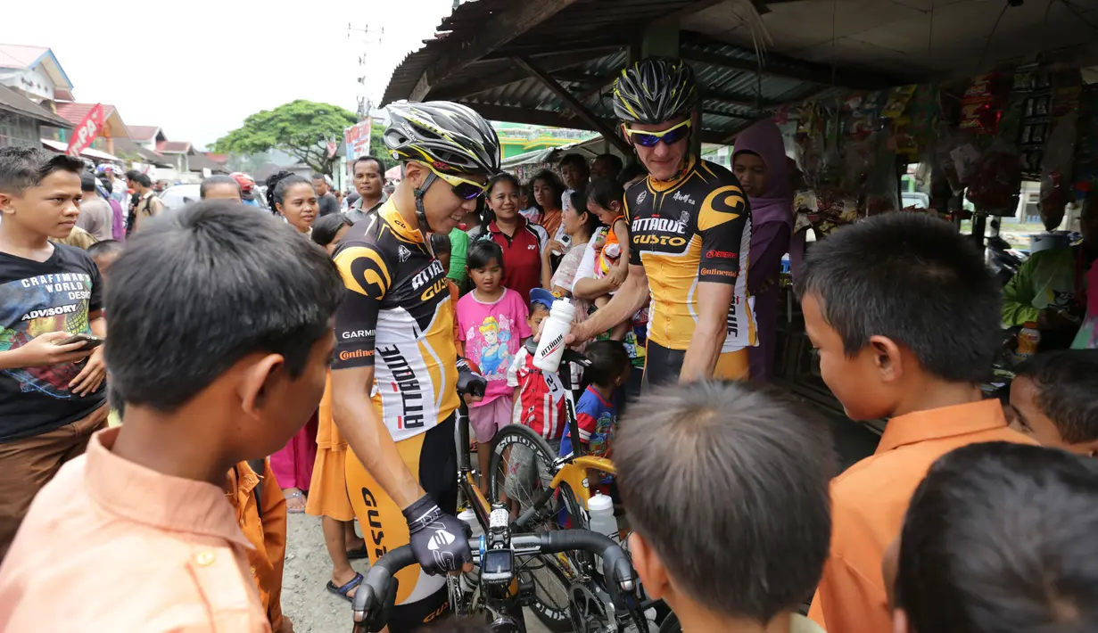 Para pebalap sepeda menjadi pusat perhatian warga saat berhenti di Barung-Barung Belantai dalam Etape 1 Tour de Singkarak antara Painan, Kabupaten Pesisir Selatan menuju Pariaman, Sumatra Barat saat, Sabtu (3/10/2015). (Bola.com/Arief Bagus)