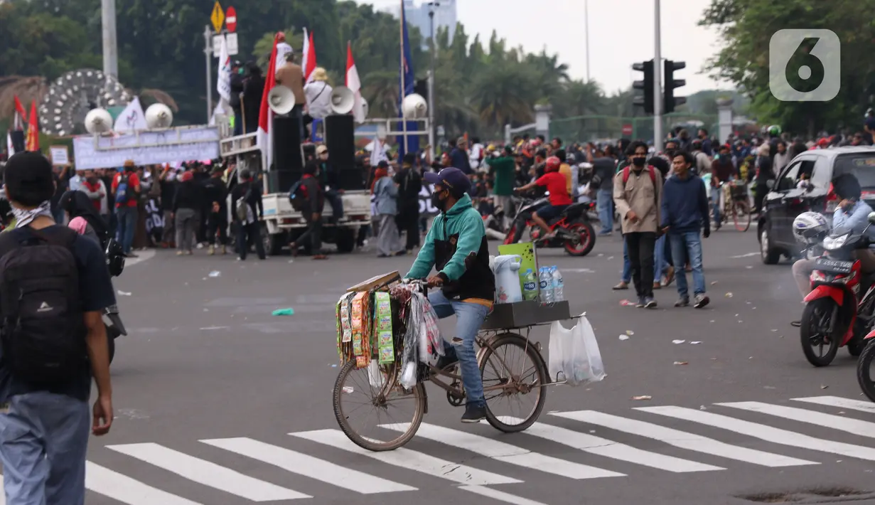 Pedangang menawarkan dagangannya kepada massa aksi saat demo penolakan omnibus law di kawasan patung kuda, Jakarta, Selasa (20/10/2020). Para pedagang kaki lima memanfaatkan moment aksi massa untuk mencari ke untungan meskupun sangat membahayakan bagi keselamatan mereka. (Liputan6.com/Angga Yuniar)