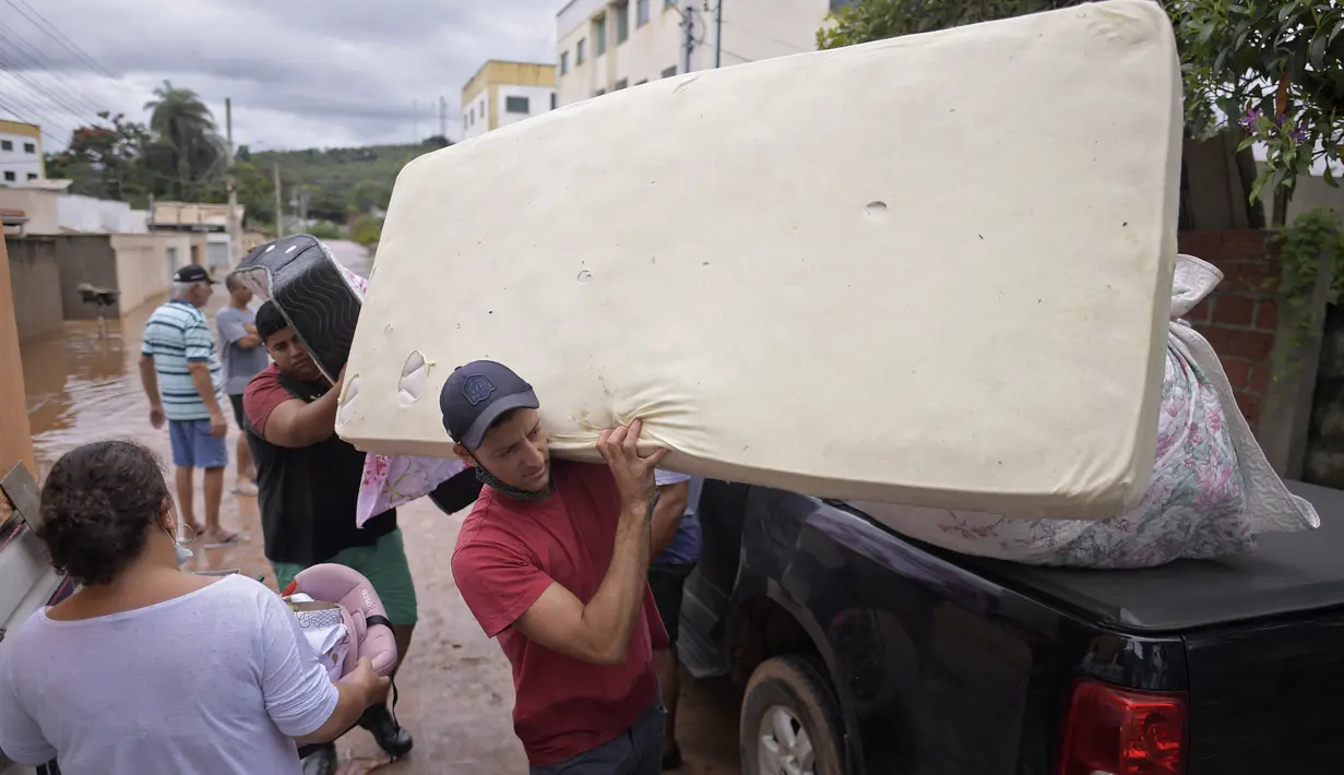 Orang-orang mengarungi air saat mereka memindahkan barang-barang dari rumah mereka yang terendam banjir di negara bagian Minas Gerais di kotamadya Juatuba, Brasil (10/1/2022). Hujan deras yang turun dalam beberapa hari terakhir di bagian tenggara negara itu membuat banjir besar. (AFP/Douglas Magno)