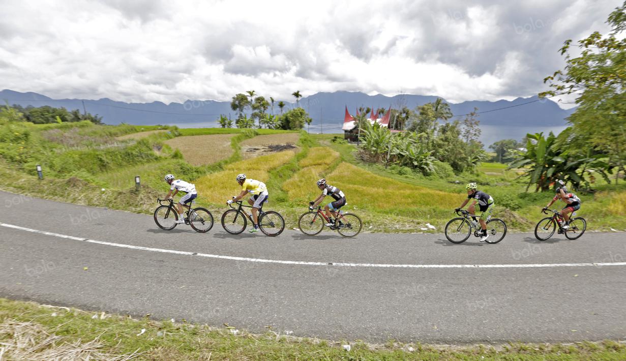 Para pebalap melintasi sawah dan Rumah Gadang pada jalur kelok 44  etape ke-4 Tour de Singkarak 2016 di Kabupaten Agam, Sumatera Barart. (Bola.com/NIcklas anoatubun)