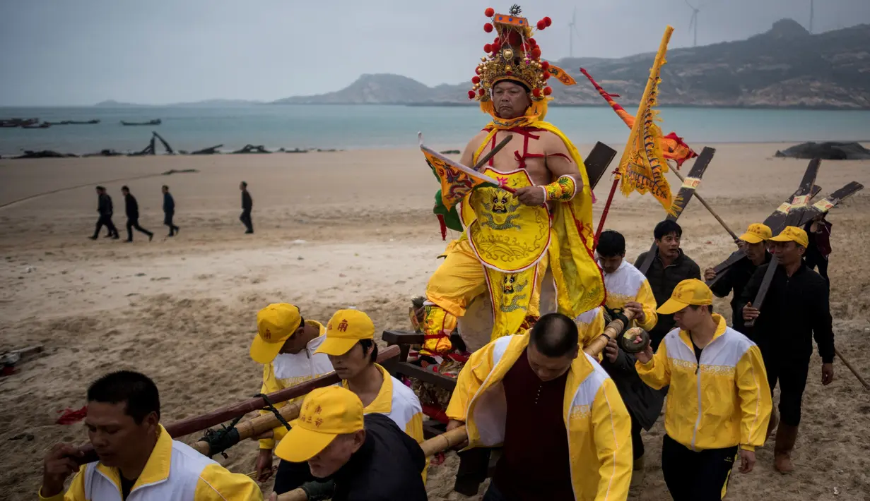 Penduduk desa menggunakan tandu membawa seorang pria berpakaian seperti Dewa Laut menuju pantai desa Fuye, Provinsi Fujian, Tiongkok (5/3). Mereka adalah komunitas nelayan setempat yang menggelar ritual kepercayaan. (AFP Photo/Johannes Eisele)