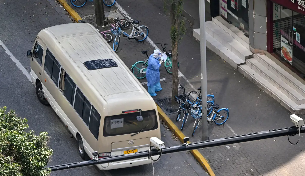 Seorang petugas kesehatan yang mengenakan alat pelindung diri berdiri sebelah bus Changning Covid Controls di depan pintu masuk ke lingkungan saat lockdown tahap kedua akibat COVID-19 di Distrik Jing'an, Shanghai, China, Rabu (6/4/2022). (Hector RETAMAL/AFP)