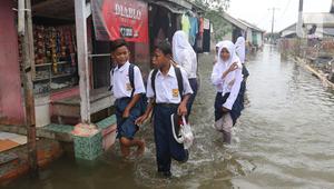 Anak-anak sekolah menerobos banjir rob yang menggenangi rumah dan tambak warga di Desa Pantai Mekar, Muaragembong, Kabupaten Bekasi, Jawa Barat, Senin (6/12/2021). Banjir rob telah menggenangi wilayah tersebut selama empat hari akibat kenaikan permukaan air laut. (Liputan6.com/Herman Zakharia)