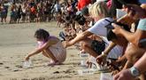 Turis berbaris saat melepaskan bayi penyu ke laut di Pantai Kuta, Bali, Indonesia, 17 Agustus 2022. Sekitar 400 penyu Lekang yang baru menetas dilepaskan saat kampanye untuk menyelamatkan penyu yang terancam punah. (AP Photo/Firdia Lisnawati)
