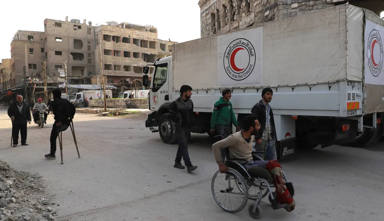 Orang-orang lalu lalang di sekitar truk bantuan yang memasuki wilayah Douma, Ghouta Timur, Damaskus, Suriah, Senin (5/3). Badan Urusan Pengungsi PBB atau UNHCR mengatakan, konvoi terdiri dari 46 truk. (AFP PHOTO/AMER ALMOHIBANY)