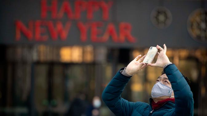 Seorang pria mengenakan masker saat mengambil foto dekorasi perayaan Imlek Tahun Tikus Logam di Beijing, 22 Januari 2020. Otoritas kesehatan China mendesak orang-orang menghindari keramaian dan pertemuan publik di Wuhan, kota yang menjadi pusat penyebaran wabah virus corona. (AP/Mark Schiefelbein)