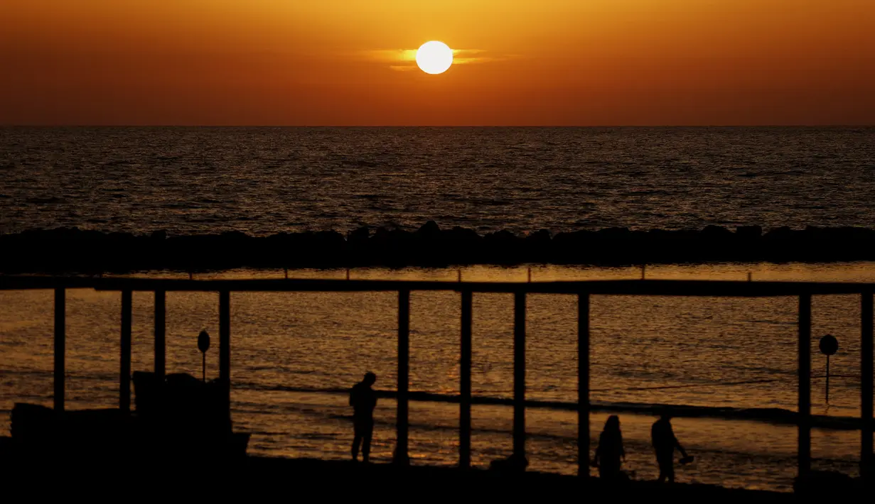 Orang-orang menyaksikan matahari terbenam di kota pesisir Mediterania Israel Netanya, utara Tel Aviv (8/6/2021). Letak kota ini yang berjarak 14 kilometer dari pantai menjadikan kota ini sebagai tempat wisata yang populer. (AFP/ Jack Guez)
