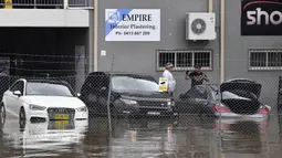 Staf Klub Olahraga Camden mengarungi banjir untuk masuk ke gedung di pinggiran barat daya Camden, Sydney, Australia, Selasa (8/3/2022). (Muhammad FAROOQ/AFP)