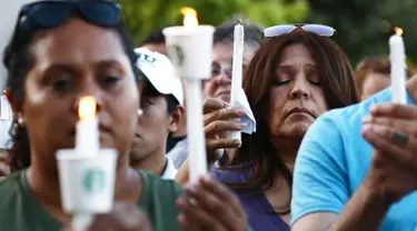 Seorang wanita berdoa sambil memegang lilin  saat menghadiri acara untuk korban penembakan brutal di festival kuliner Gilroy Garlic di Gilroy, California (29/7/2019). Tiga orang tewas dan sedikitnya puluhan orang terluka akibat kejadian tersebut. (AFP Photo/Mario Tama)