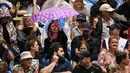 Seorang wanita berlindung di bawah payung saat hujan selama pertandingan tunggal putaran pertama antara Roger Federer dari Swiss dan Steve Johnson dari Amerika Serikat di kejuaraan tenis Australia Terbuka di Melbourne, Australia, Senin (20/1/2020). (AFP Photo/William West)