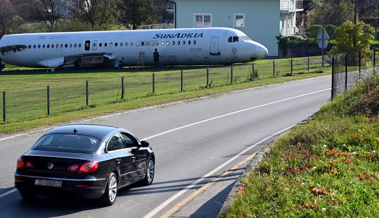 Sebuah mobil melintas dekat badan pesawat Fokker-100 yang terlihat diparkir di halaman rumah warga setempat di Strmec Stubicki, dekat Zagreb, Kroasia, 26 Oktober 2019. Butuh enam pekan untuk merobohkan pesawat dan lima hari untuk mengangkutnya. (Denis LOVROVIC / AFP)