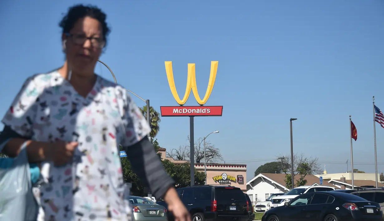 Seorang wanita berjalan dengan latar belakang plang logo restoran cepat saji McDonald's yang terbalik di Lynwood, California (8/3). Huruf W tersebut merupakan inisial untuk women atau wanita. (AFP Photo/Frederic J. Brown)