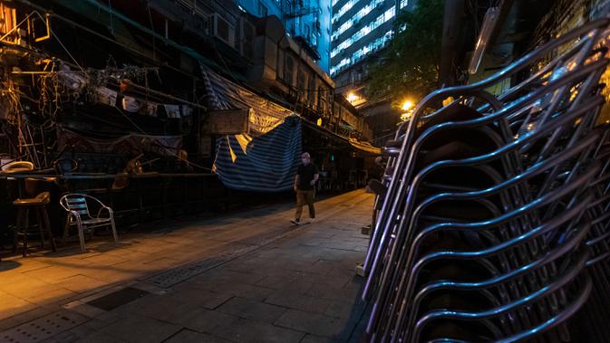 Seorang pria mengenakan masker pelindung melintas di jalanan sepi di kawasan hiburan malam Lan Kwai Fong, Hong Kong (5/5/2020). Kebijakan pemerintah Hong Kong itu membuat gemerlap hiburan malam di Lan Kwai Fong meredup seketika. (AFP/May James)